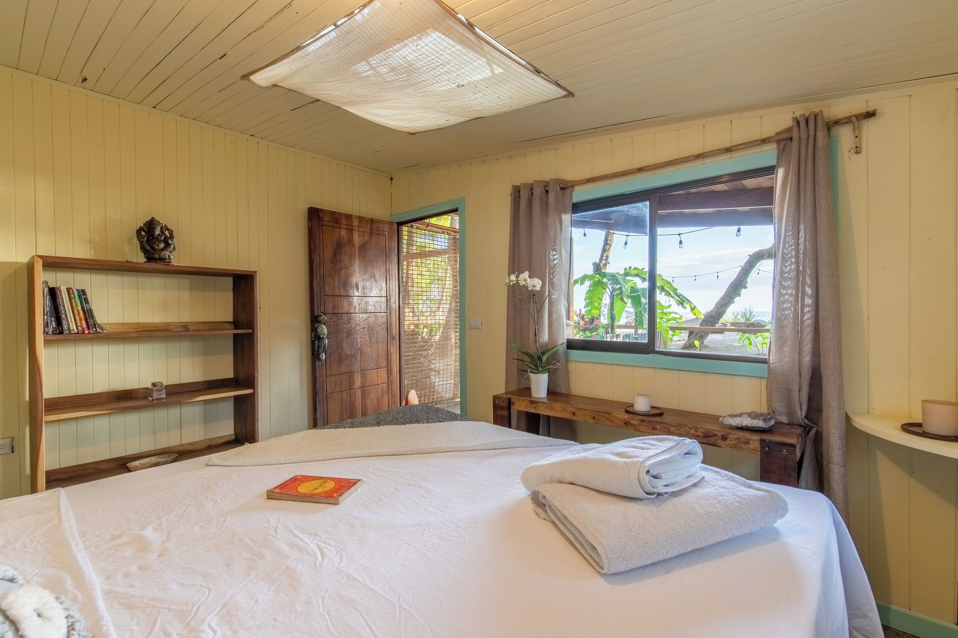 Habitación de hotel con cama, estantería, ventana con cortinas y vista a zonas verdes.