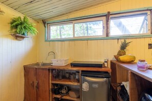 A compact kitchen with a sink, a refrigerator, and a window with a view of trees.