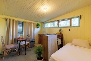 A room with a bed, a table with chairs, a small sink, and a window with curtains.
