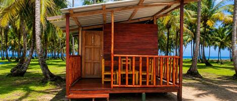 A wooden structure with a porch, a door, and a view of the beach and palm trees.
