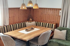 A wooden dining table with a white placemat, surrounded by striped upholstered benches and chairs. - Schartner Rosi House (Kleinarl)