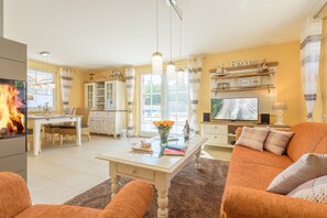 A living room with a fireplace, a television, and a dining area with a table and chairs. - Holiday home in Glowe with swimming pool (Glowe)