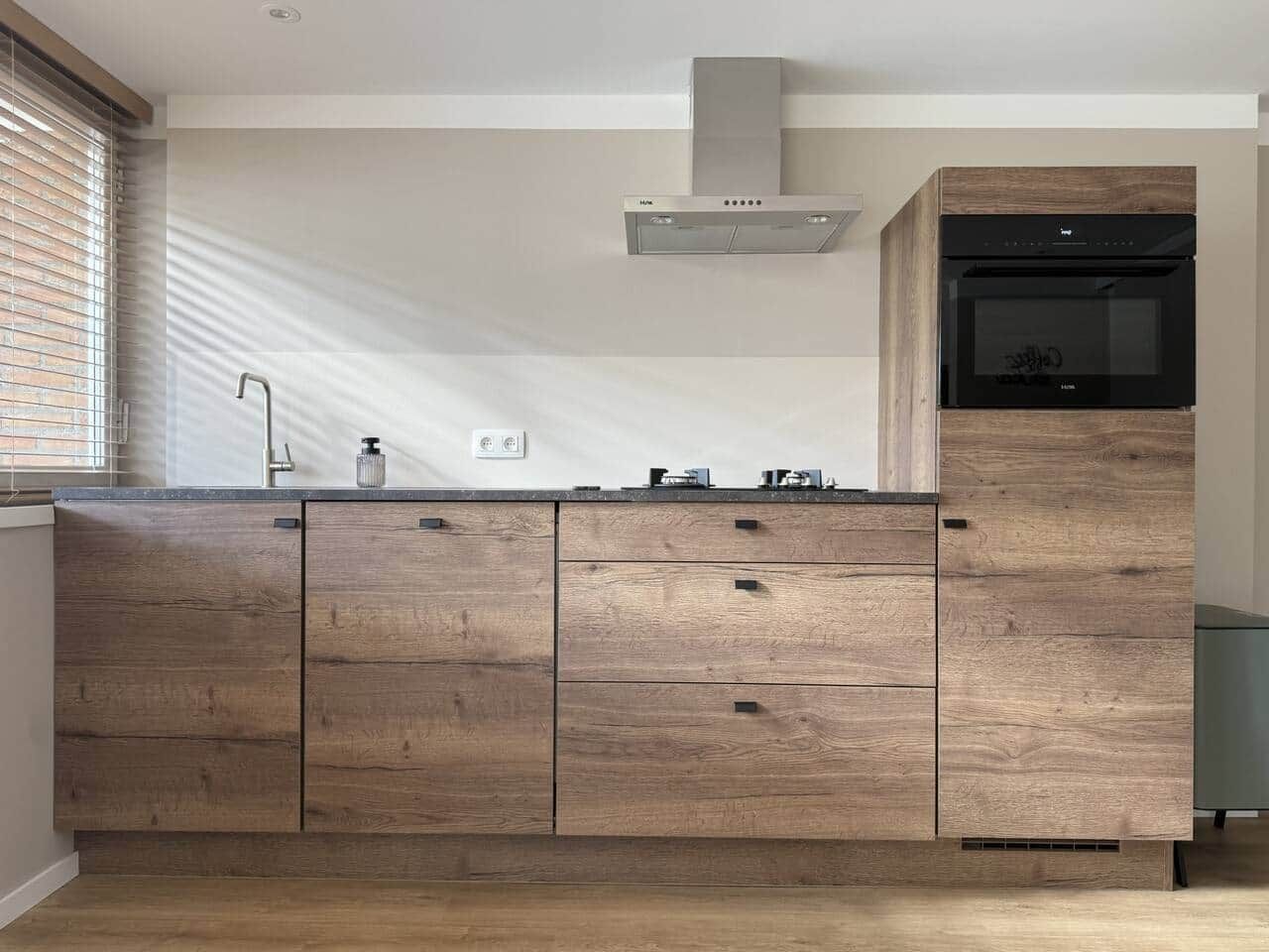 A modern kitchen with wooden cabinets, a stainless steel range hood, and a built-in microwave.