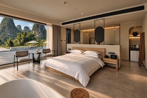 Habitació d'hotel moderna amb un llit gran, zona de seients amb taula i cadires, petita cuina i vista a un paisatge de muntanya.