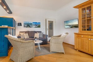 A living room with a sofa, two wicker chairs, a small table with a bottle and glass, a cabinet, and two wall-mounted pictures. - Baltic Sea view in the Villa Stranddistel (Binz)