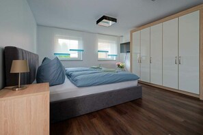 Et moderne soveværelse med seng, sengebord, lampe, garderobeskab og vinduer.