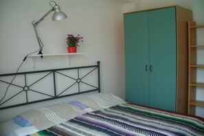 Ein Schlafzimmer mit einem Bett, einer Schreibtischlampe, einem Regal mit einer Topfpflanze und einem türkisblauen Kleiderschrank.