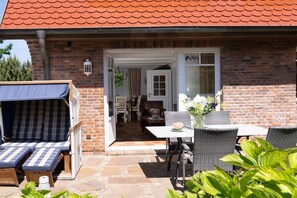 Ein Backsteinhaus mit rotem Ziegeldach, einer Terrasse mit Gartenmöbeln und einer Tür, die in einen Innenraum führt.