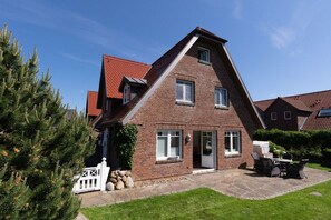 Ein zweistöckiges Backsteinhhaus mit Satteldach, einer Veranda und einer Terrasse mit Gartenmöbeln.