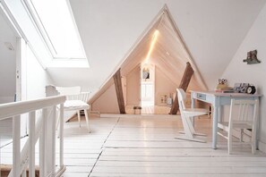 A room with a sloped ceiling, white walls, and a wooden floor. There is a desk with chairs and a window. - country house style in Heiligenhafen (Heiligenhafen)