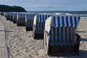 Eine Reihe von Liegen reiht sich an einem sandigen Strand auf, im Hintergrund das Meer.