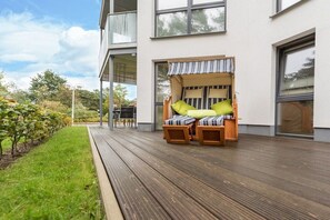 Ein moderner Außenbereich mit Holzterrasse und überdachtem Sitzbereich mit gestreiften Kissen.