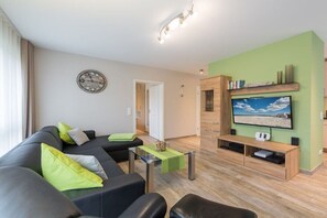 Ein modernes Wohnzimmer mit einer Couch, einem Couchtisch, einem Fernseher und einem Bücherregal.