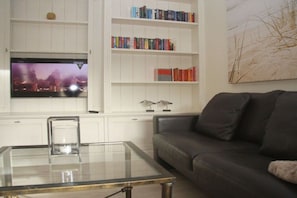 A living room with a flat-screen TV, a glass coffee table, a leather sofa, and a bookshelf with books. - 1 in the Annelene house (Westerland\/ Sylt)