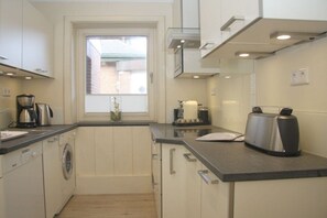 A compact kitchen with a washing machine, a toaster, and a window with a view of a building outside. - 1 in the Annelene house (Westerland\/ Sylt)