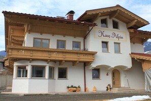 Ein zweistöckiges Gebäude mit einem Schild, auf dem 'Haus Alpina' steht. Es hat einen Balkon mit Holzgeländern und ein rotes Ziegeldach.