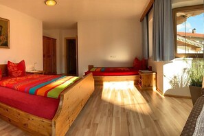 Ein Zimmer mit zwei hölzernen Betten, einem fenster mit Vorhängen und Blick auf ein Gebäude.