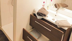 Un baño con ducha, lavamanos con espejo y un perchero para toallas.