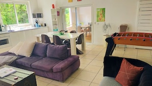 Una sala de estar con un sofá púrpura, una mesa de centro, una mesa de fútbol de mesa y un comedor con sillas y una mesa.