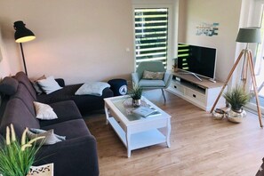 A modern living room with a sofa, armchair, coffee table, TV, and floor lamp. - Holiday apartment with 2 bedrooms (Grömitz)