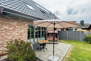 Eine Terrasse mit Tisch und Stühlen, einem großen Sonnenschirm und einem Ziegelhaus mit Ziegeldach.