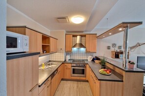 A modern kitchen with wooden cabinets, a stainless steel range hood, and a built-in microwave. - Holiday apartment with 2 bedrooms (Warnemünde)