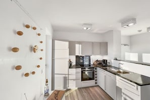 A modern kitchen with white cabinetry, a black countertop, and a built-in oven. - Holiday apartment in Glowe with swimming pool (Glowe)
