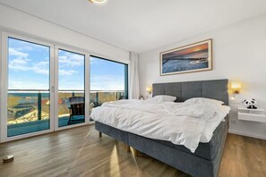 Une chambre avec un grand lit, une vue par une porte coulissante et un tableau au mur.