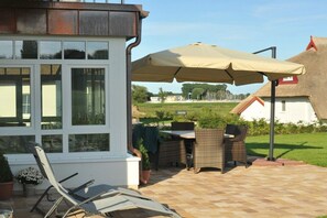 Eine Terrasse mit Gartenmöbeln, einem Tisch und einem großen Sonnenschirm.