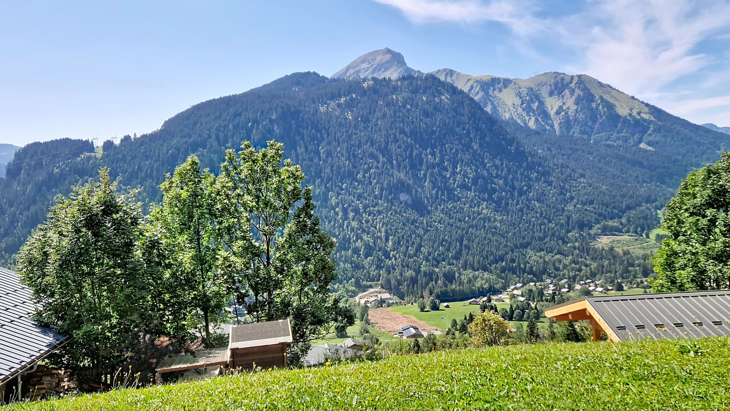 Un paisaje montañoso con un pueblo en el valle, casas con techos inclinados y colinas boscosas y densas.