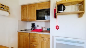 A compact kitchen with wooden cabinets, a microwave, a coffee maker, and a red hanging ornament. - AGA2 VIEW & MOUNTAIN Alpine Chalet (3 People) (Châtel)