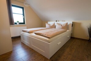 A bedroom with a sloped ceiling, a bed with white bedding, a radiator below the window, and a wooden floor. - Holiday home in Lübbenau with swimming pool (Lübbenau)