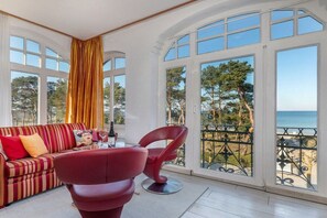 A room with a sofa, a chair, and large windows overlooking a beach. - Sorrento, Villa Glückpilz (Binz)
