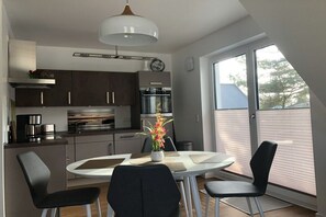 Une cuisine moderne avec des meubles de couleur sombre, un plan de travail blanc et un coin repas comprenant une table ronde et quatre chaises.