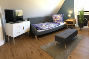 Ein modernes Schlafzimmer mit einem Bett, einem Fernseher, einem Nachttisch, einer Lampe und einer Topfpflanze.