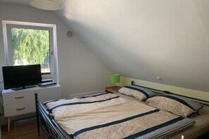 Quarto com cama, televisão em escrivaninha e janela com vista para árvores.