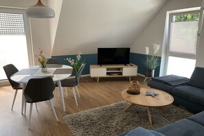A modern living room with a dining area, a flat-screen TV, and a sofa. - Holiday apartment with 2 bedrooms (Zinnowitz)
