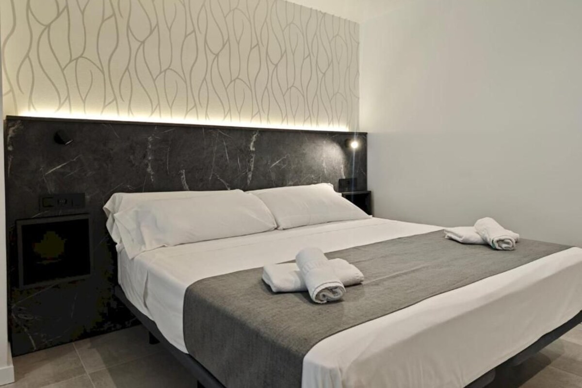 Una camera d'albergo moderna con un letto grande, una testiera dal motivo originale e un comodino con una lampada.