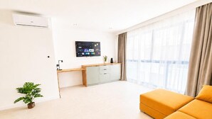 Uma sala de estar moderna com um sofá, uma TV de tela plana, um pequeno armário e um vaso com planta.