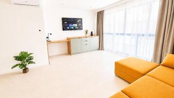 Una sala de estar moderna con un sofá, un televisor de pantalla plana, un mueble bajo y una planta en maceta.