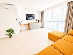Un soggiorno moderno con un divano, una TV a schermo piatto, un piccolo mobiletto e una pianta in vaso.