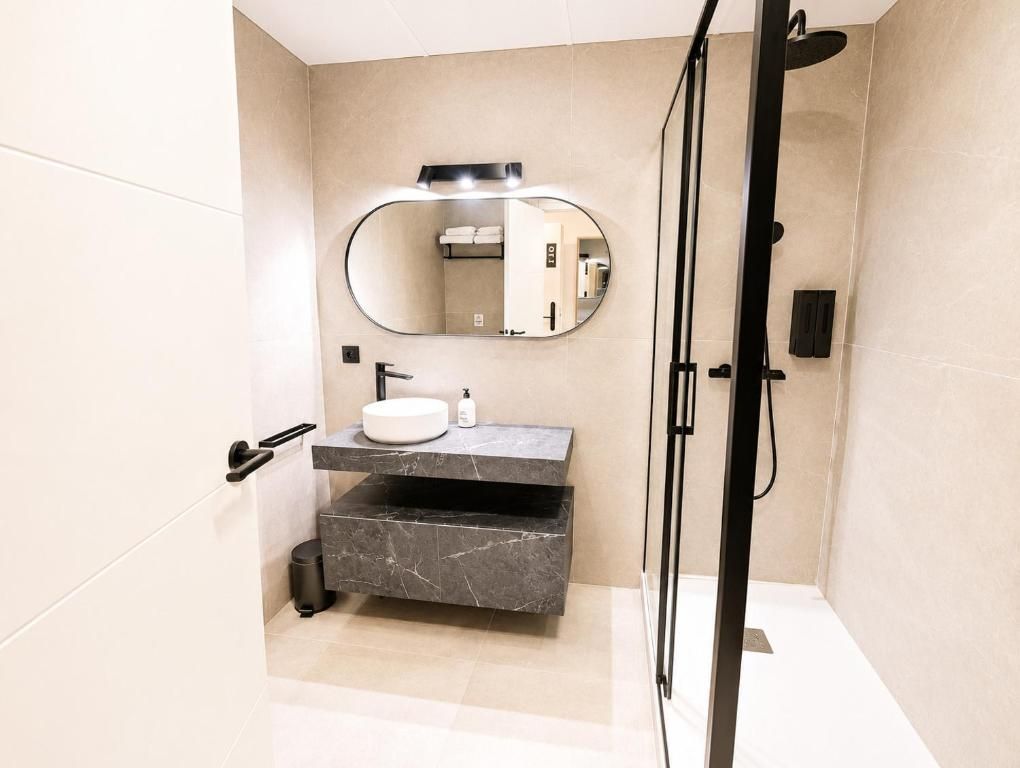 Un baño moderno con tocador de mármol, un espejo redondo y cabina de ducha.