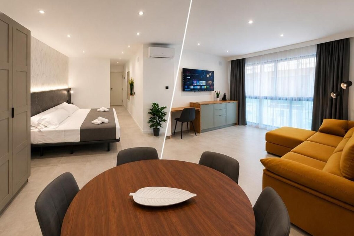 Una camera d'hotel moderna con un letto, un tavolo da pranzo con sedie, un divano, una scrivania con sedia e una TV a parete.