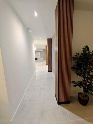 Un pasillo con un separador de madera, una planta en maceta y piso de baldosas.