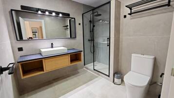 Un baño moderno con ducha envuelta en vidrio, inodoro blanco y tocador con espejo e iluminación.