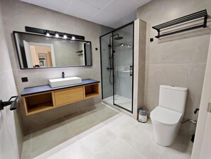 Un bagno moderno con cabina doccia in vetro, un WC bianco e un mobile lavabo con specchio e illuminazione.