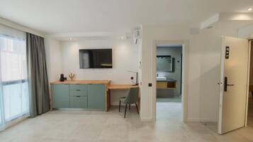 Een moderne hotelkamer met een kitchenette, bureau en televisie.