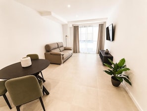 Una sala de estar moderna con un sofá, una mesa de comedor con sillas, un televisor de pantalla plana en la pared y una planta en maceta.