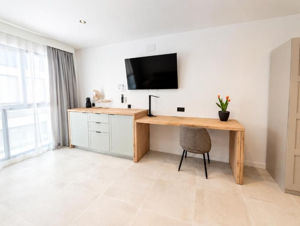 Una habitación moderna con un escritorio de madera, un televisor de pantalla plana y una planta en maceta.