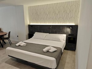 Quarto de hotel com cama, cabeceira com painel iluminado, mesa de jantar e uma cadeira.
